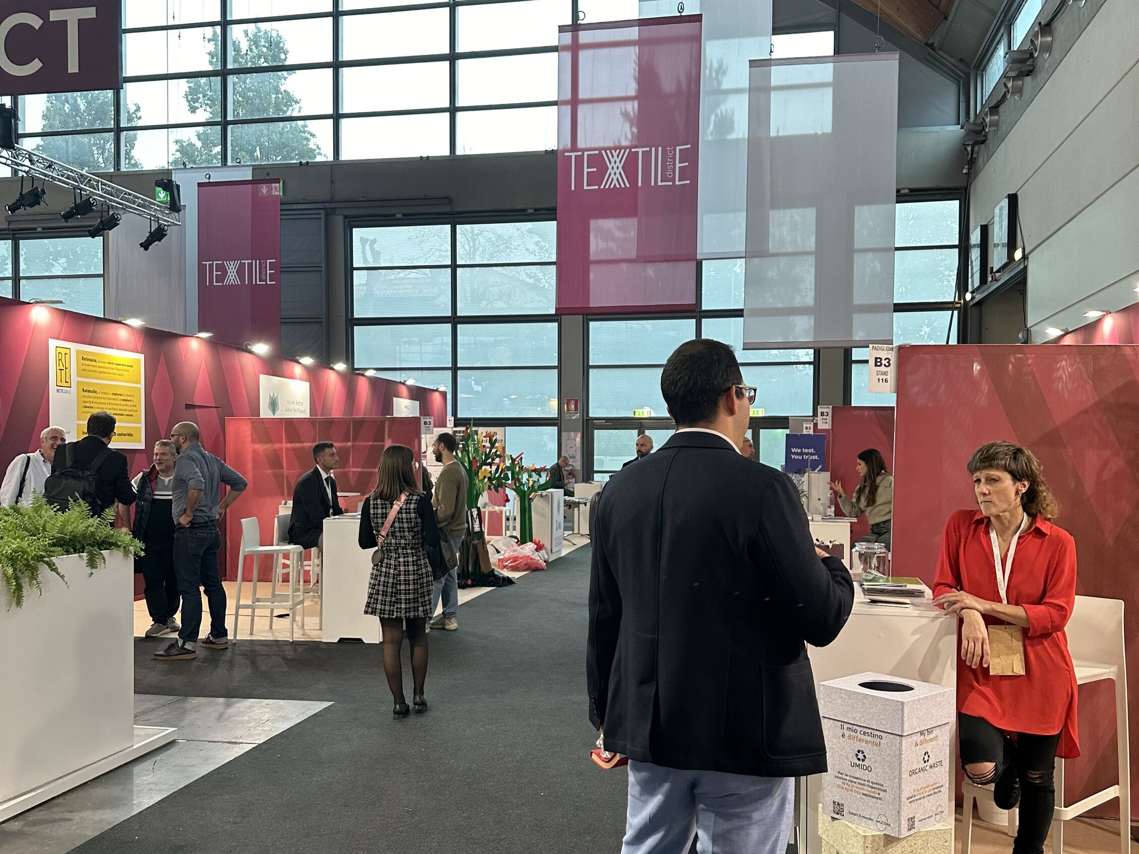 Visitors interact with exhibitors inside the 'TEXTILE' area, surrounded by colorful booths and modern decorations