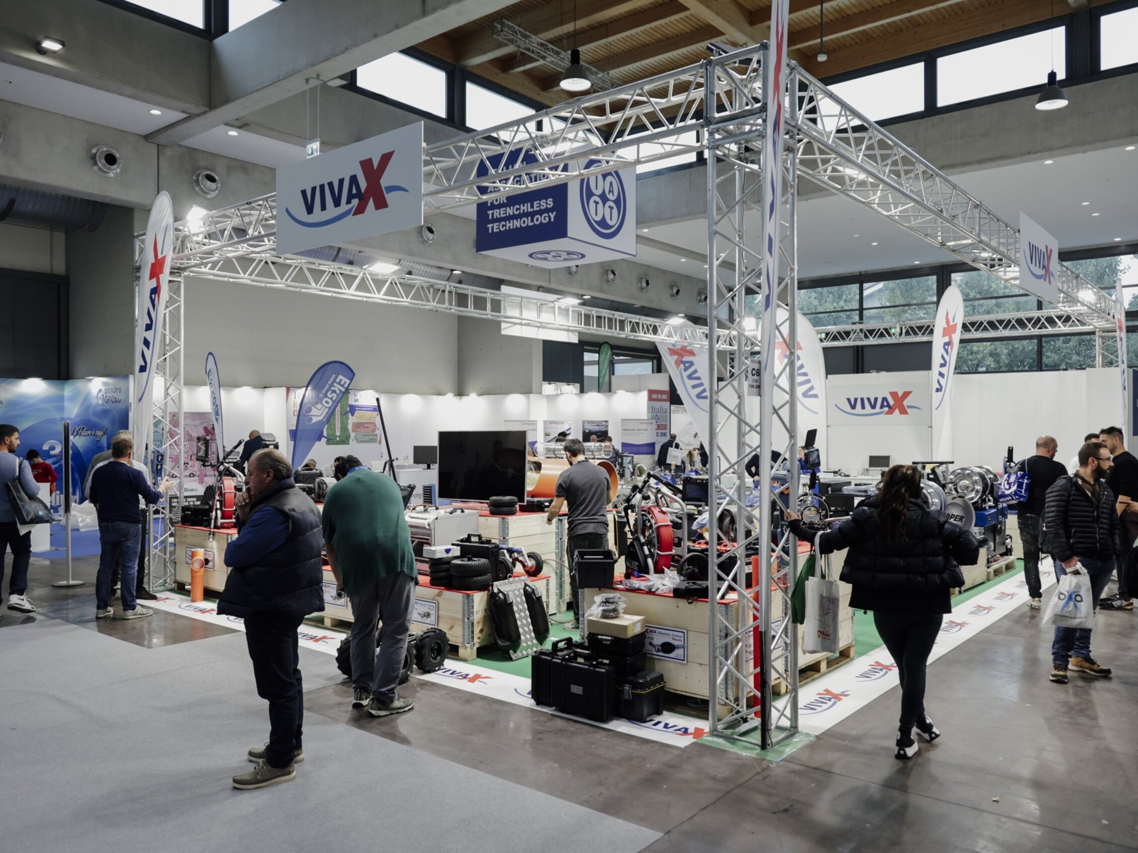 Visitatori esplorano lo stand espositivo del marchio 'VIVAX' dedicato alla trenchless technology, circondato da macchinari e attrezzature specializzate 