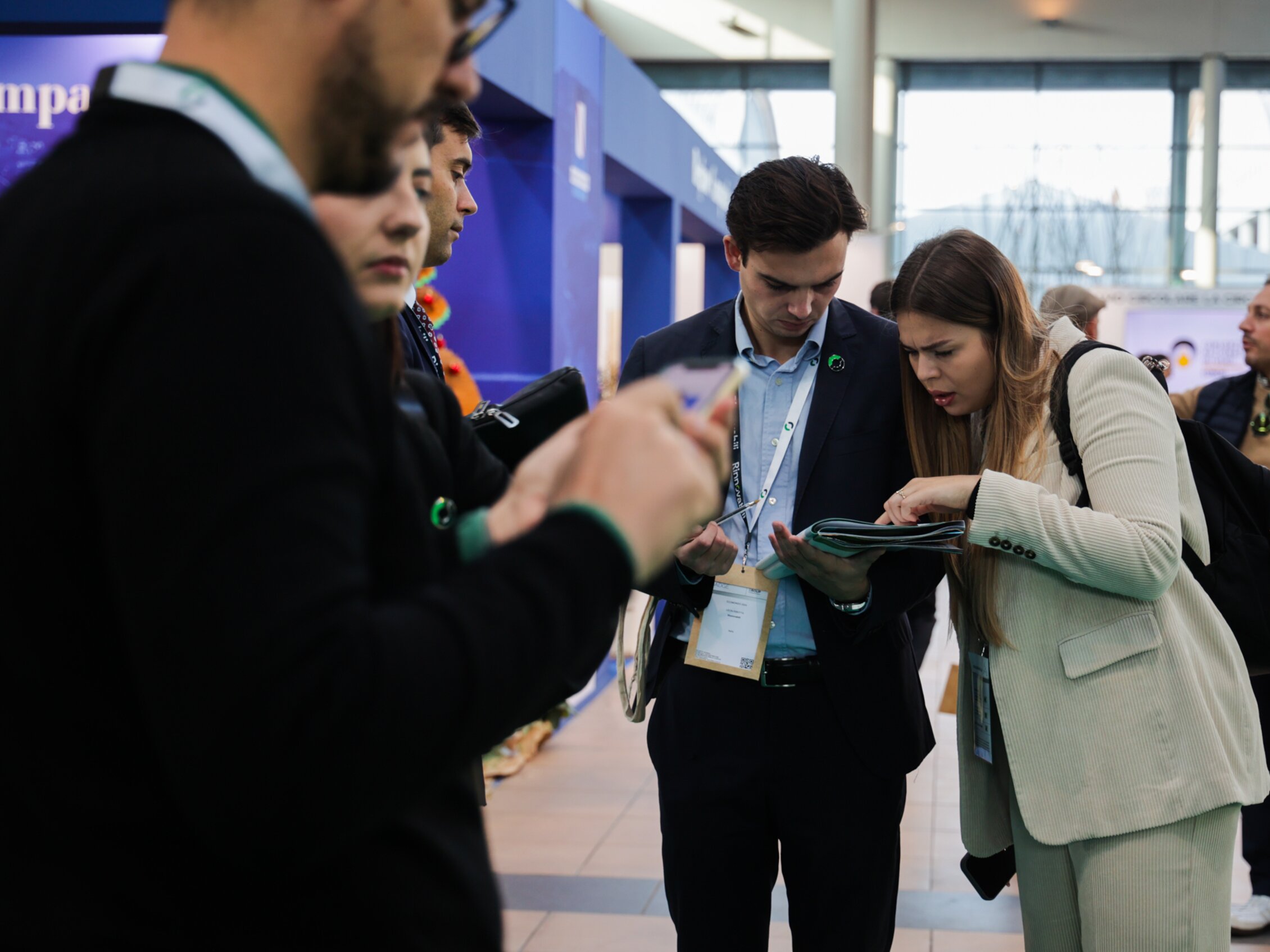 Due partecipanti consultano una brochure all’interno della fiera, circondati da altri visitatori tra gli stand espositivi