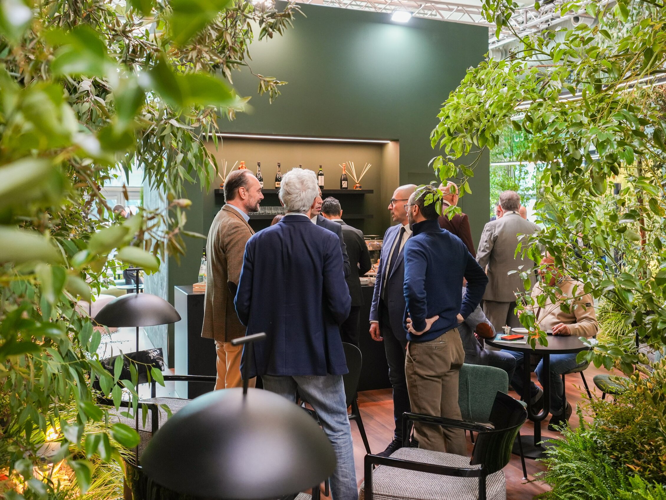 Visitatori dialogano all’interno di uno stand immerso nel verde, arredato con numerose e grandi piante ornamentali 
